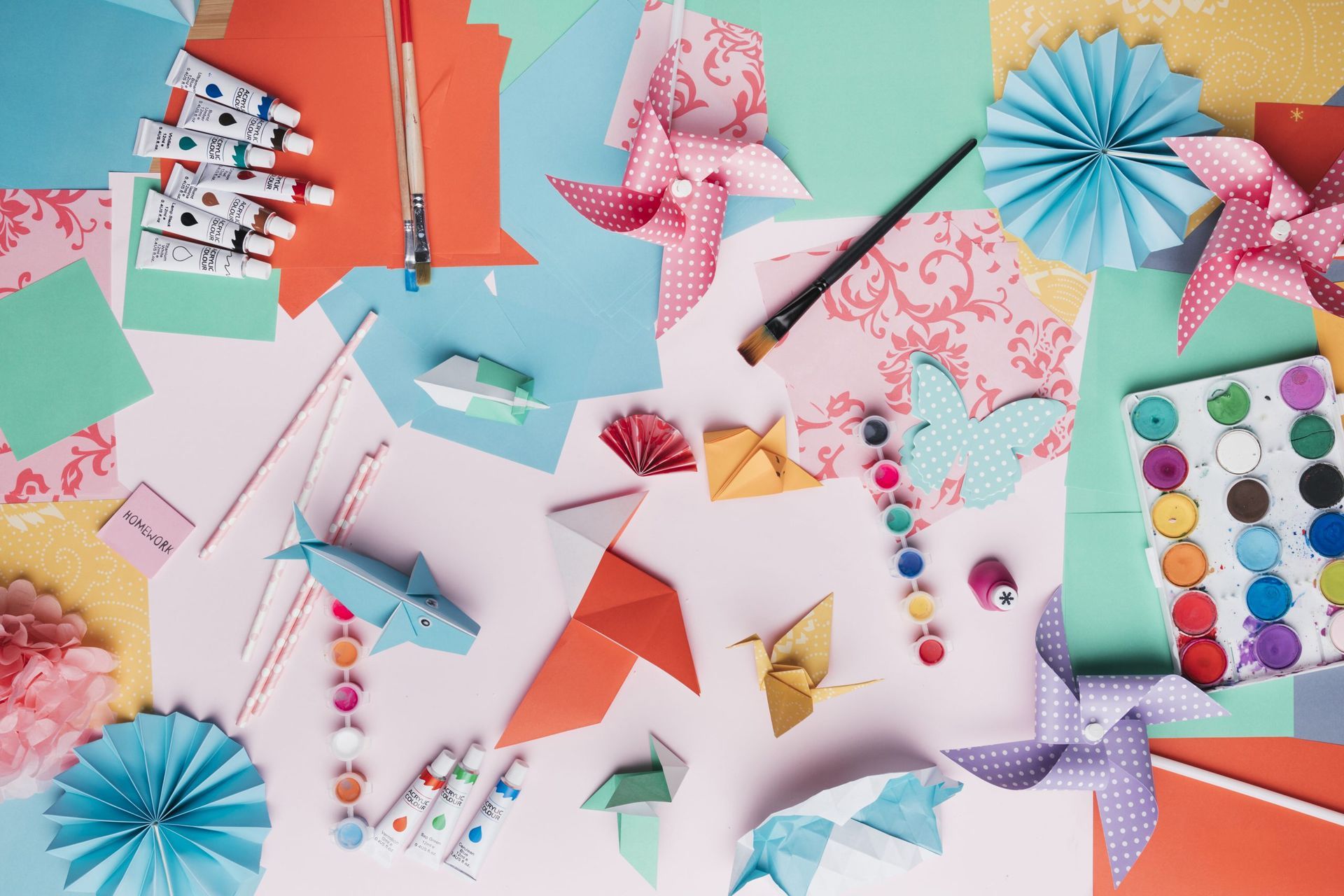 Materiali colorati per lavori creativi con la carta e pezzi di origami piegati, disposti su una superficie di lavoro dai toni pastello.