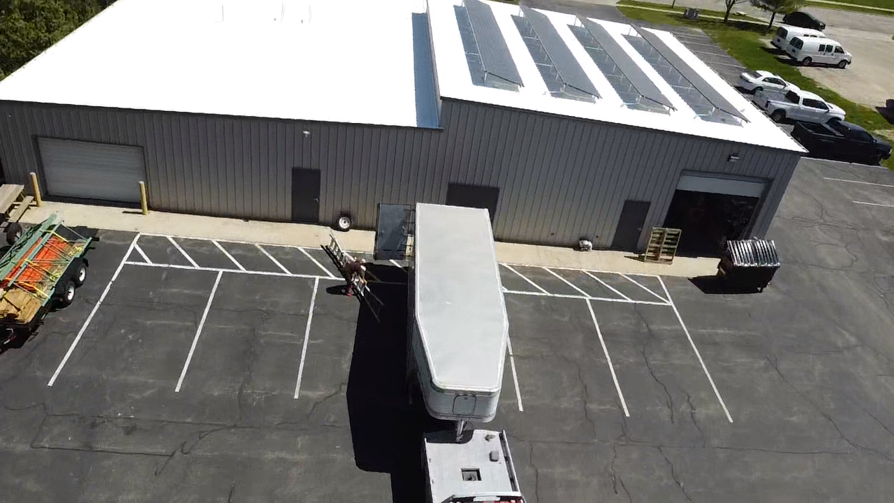 A semi-truck backing into a loading dock at a warehouse with solar panels on the roof.