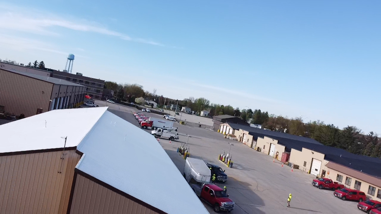 Aerial view of a commercial area with buildings, vehicles, and a water tower under a blue sky.