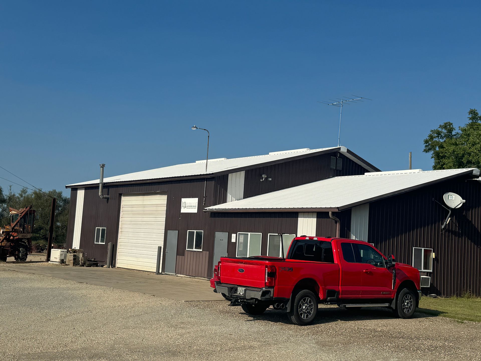 Red truck parked in front of a dark brown building with a white metal roof and a clear blue sky.