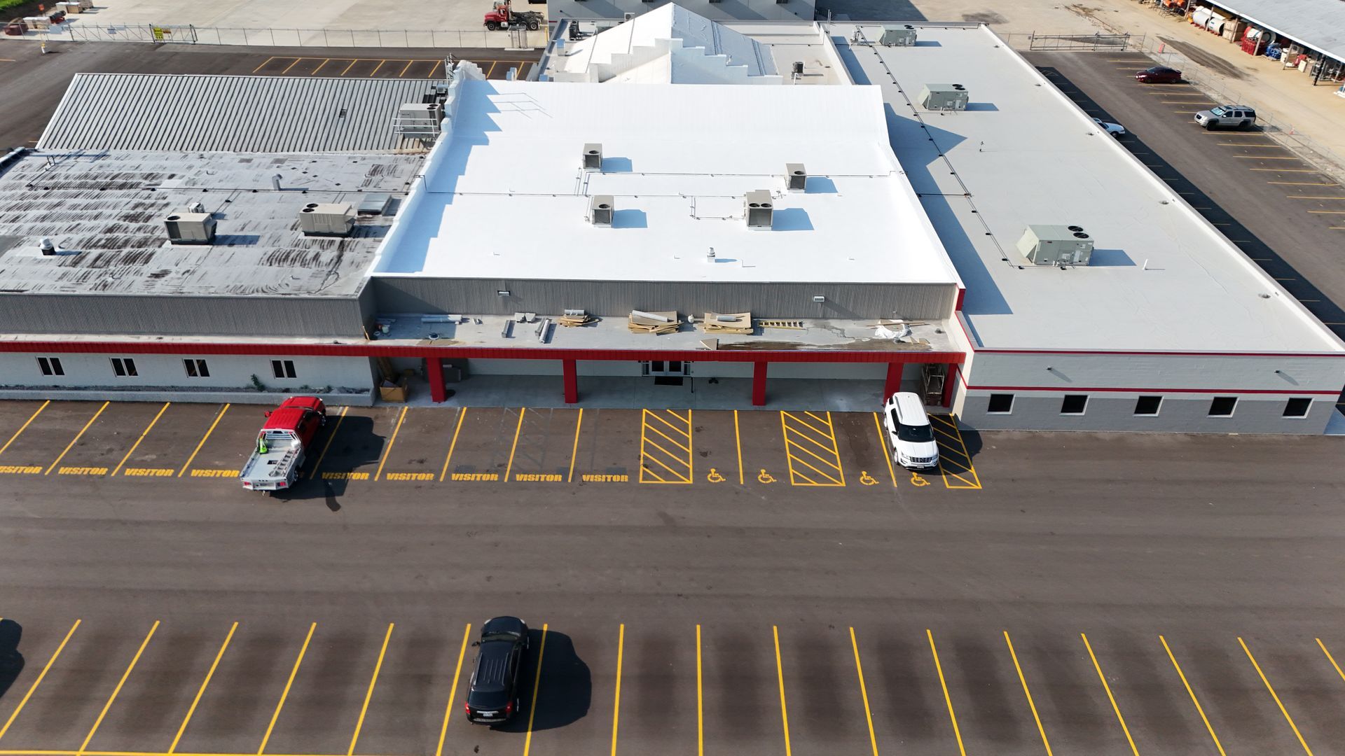 Aerial view of a commercial building with a white roof, red trim, and a parking lot with several vehicles.
