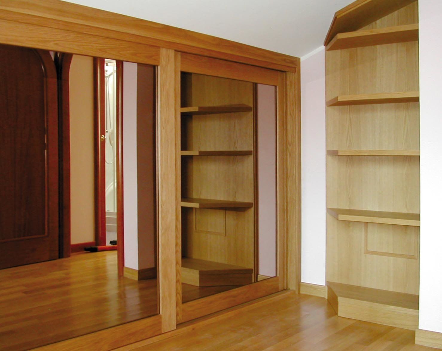 Scaffalature e armadi in legno con ripiani aperti e ante scorrevoli, posizionati su un pavimento in legno.