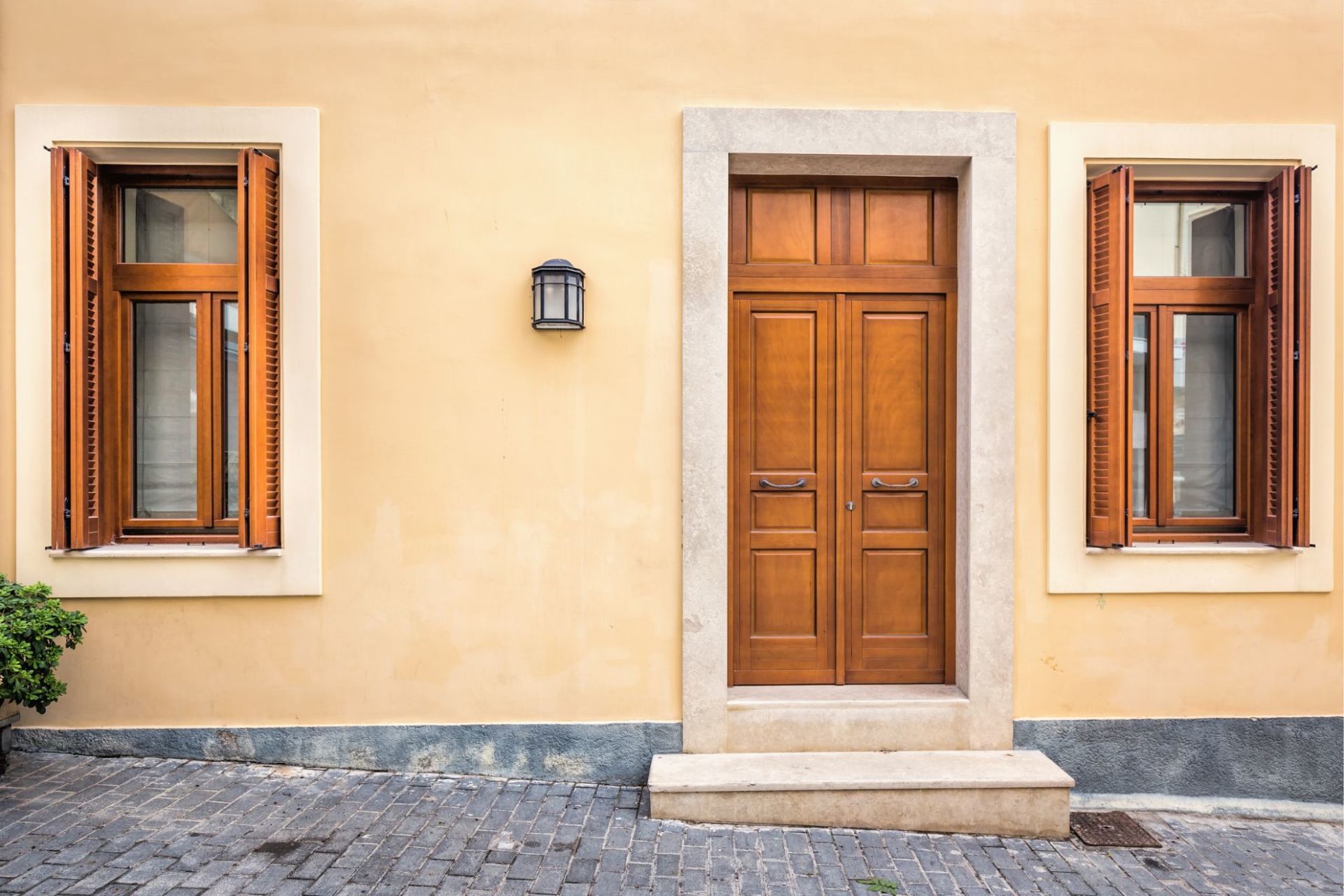 Facciata beige dell'edificio con porte e finestre in legno marrone. Rifiniture in pietra. Pavimento in ciottoli.