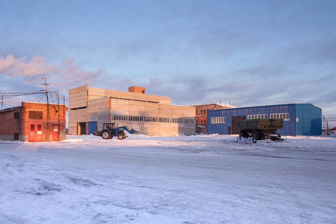 Snow-covered industrial buildings at sunset, with trucks parked in a wide open yard.