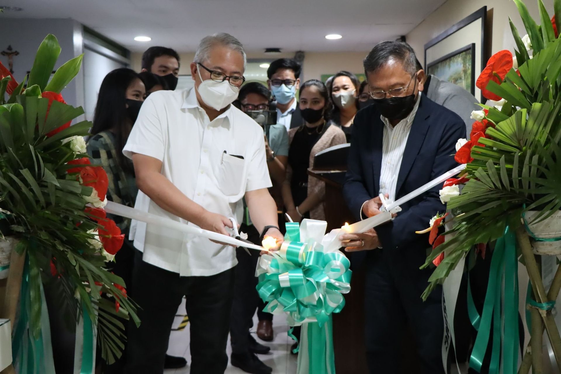 People cutting a green ribbon at an indoor ceremony with floral decorations