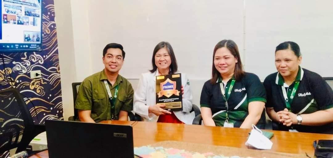 Four people seated indoors at a table, smiling and holding a book in a meeting room
