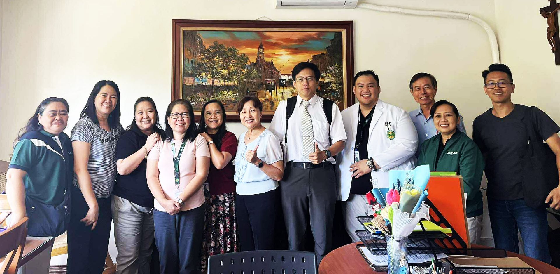 Group of people standing indoors in an office, posing behind a table with flowers and documents