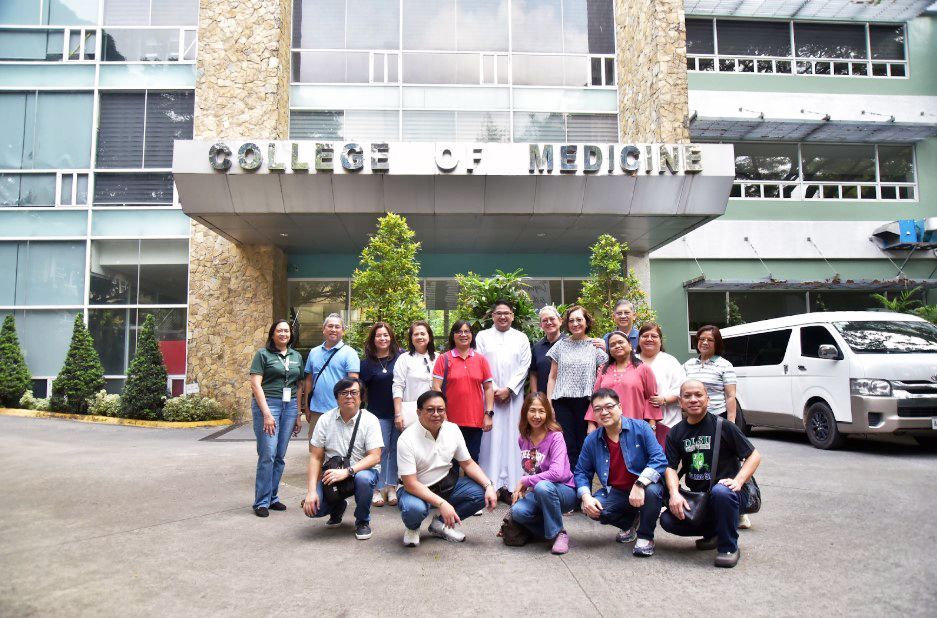 Group of people posing outside a college of medicine building with a parked white van nearby