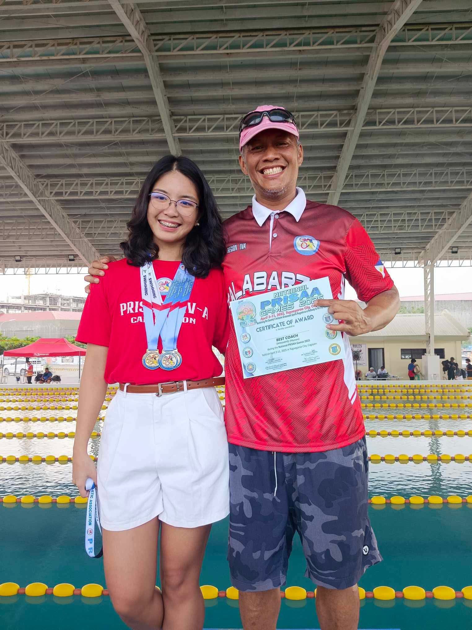 Two people in red jerseys holding a certificate, standing under a covered sports venue.