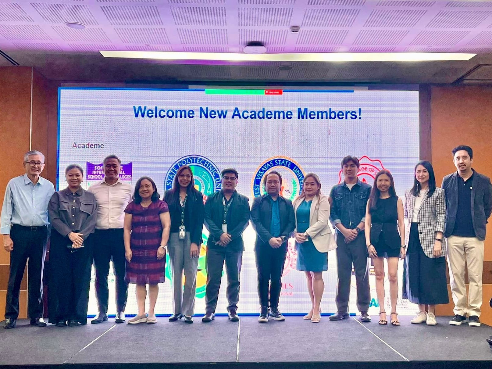 Group of people posing onstage under a “Welcome New Academe Members!” banner