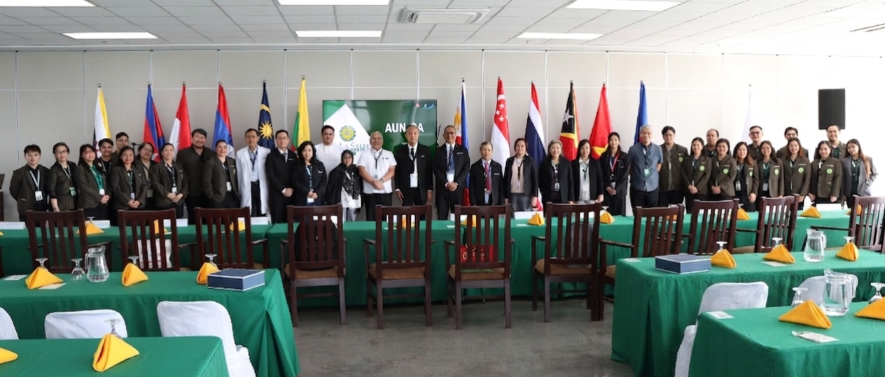 Group of people posing indoors at a formal event, with flags and green tablecloths in the foreground.