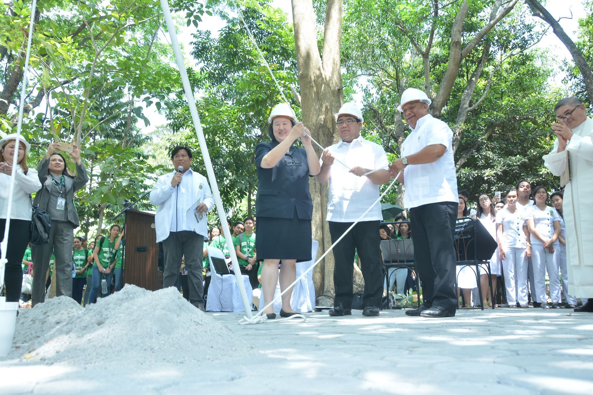 People shoveling white powder at an outdoor ceremonial event under trees