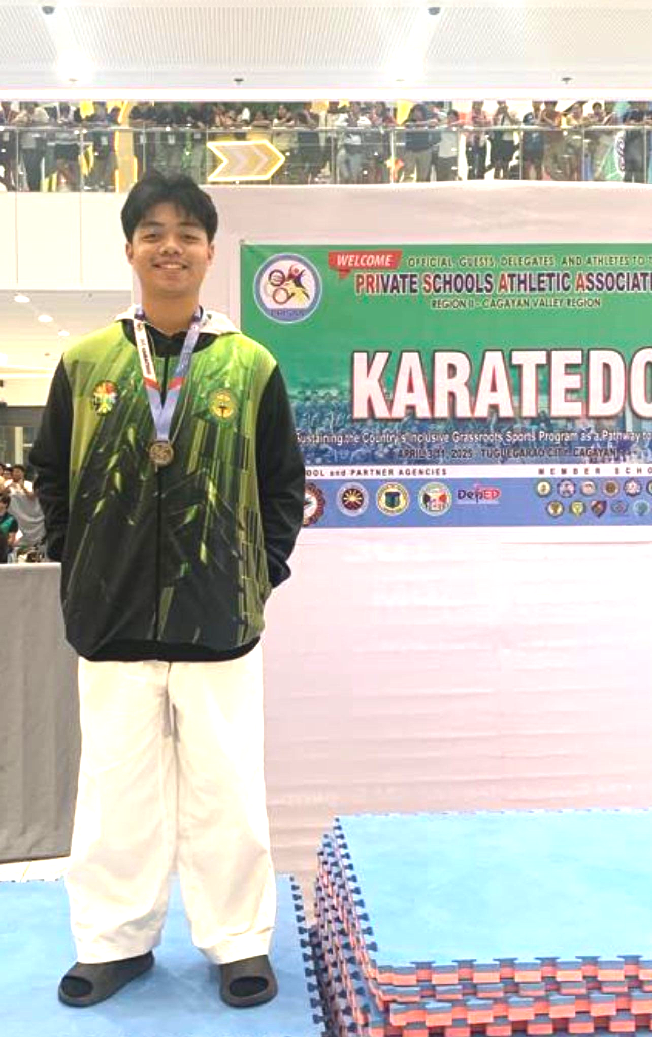 Person in green jacket and white pants standing on a podium at a karate competition.