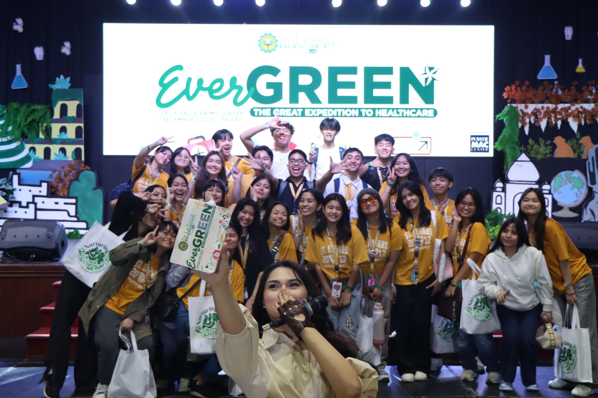 Group of smiling people posing onstage in front of an “EverGREEN” banner, many holding signs.