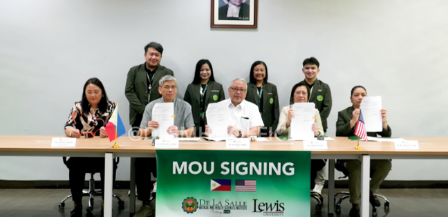 People seated at a table during a MOU signing event with a green banner reading “MOU SIGNING.”