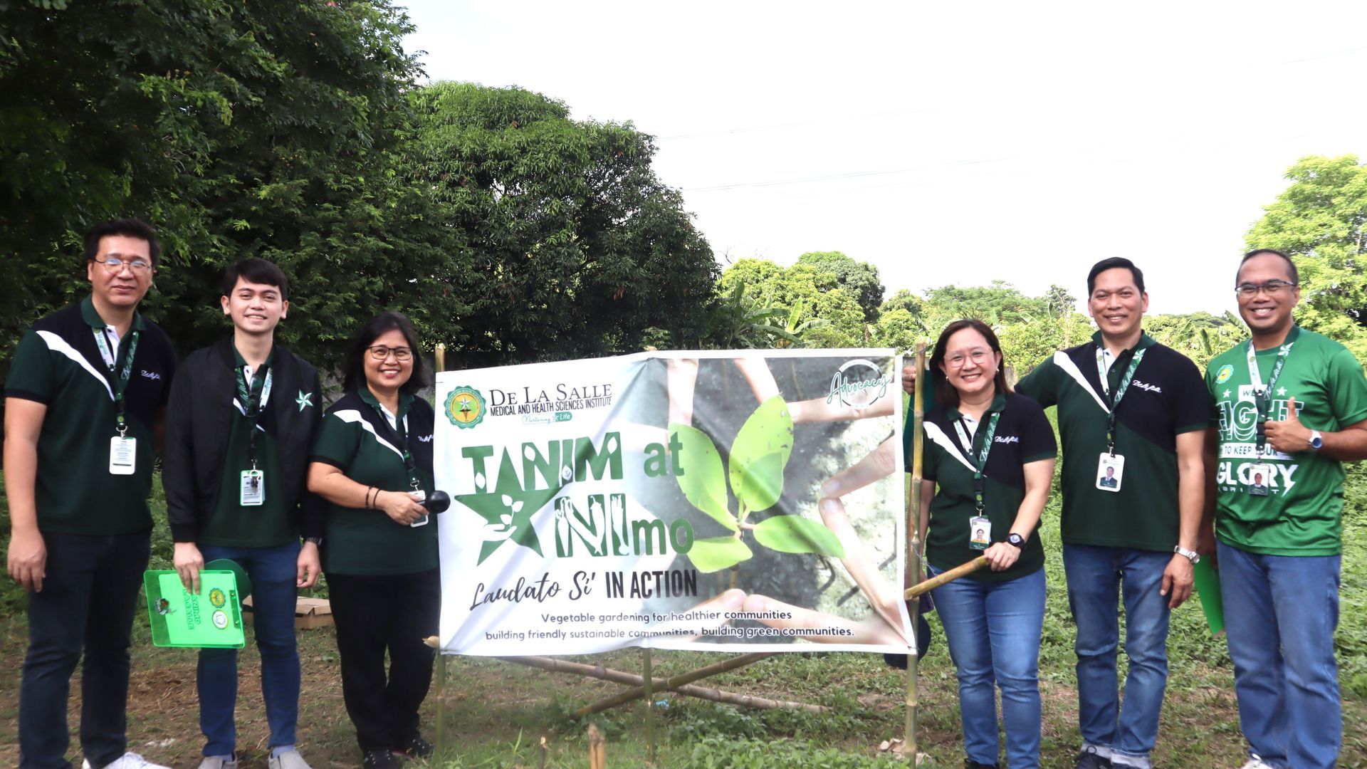 Group of volunteers holding a banner in a green outdoor park setting, smiling at the camera