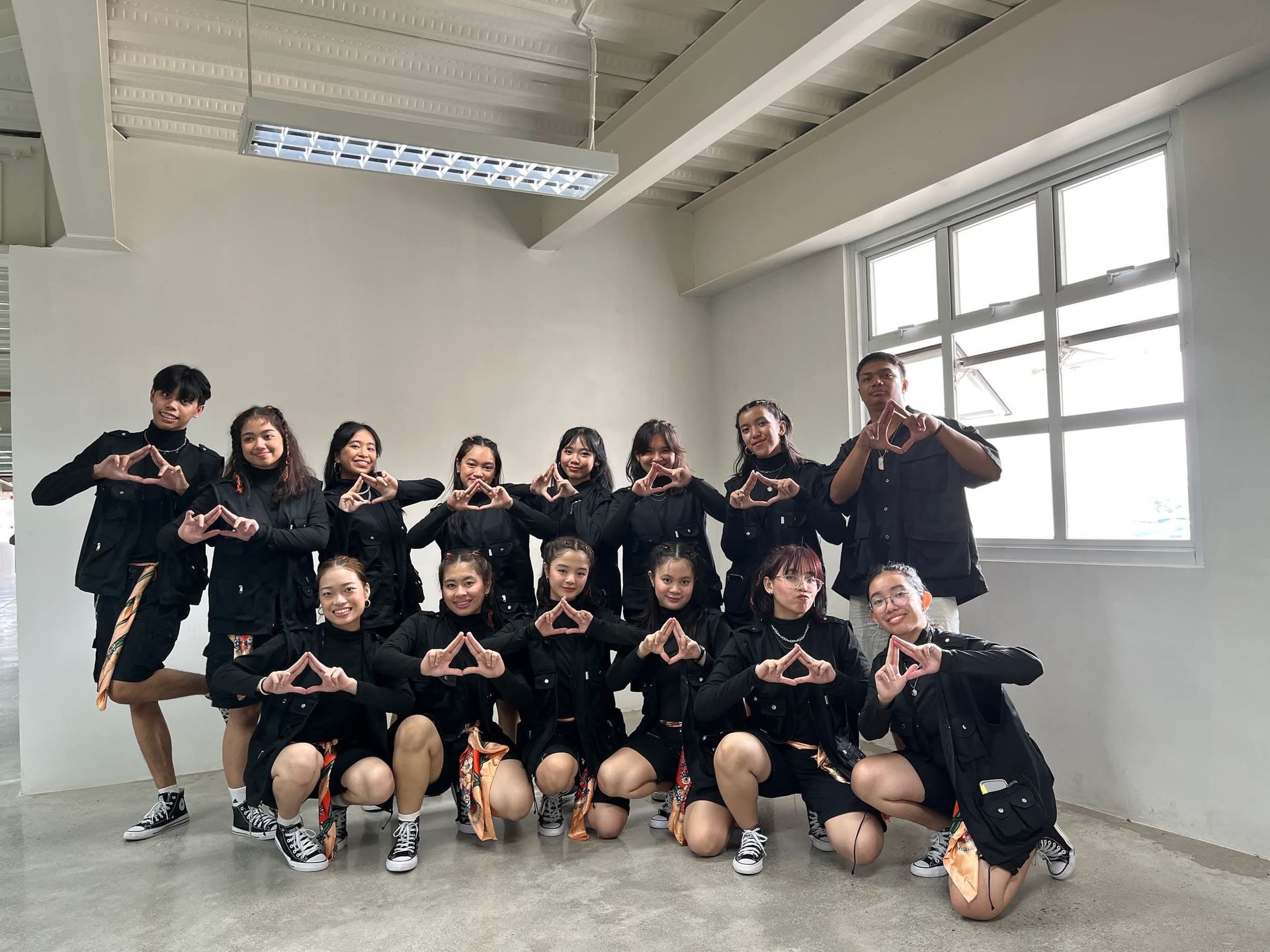 Team group posing in a bright studio, dressed in black and making hand gestures.