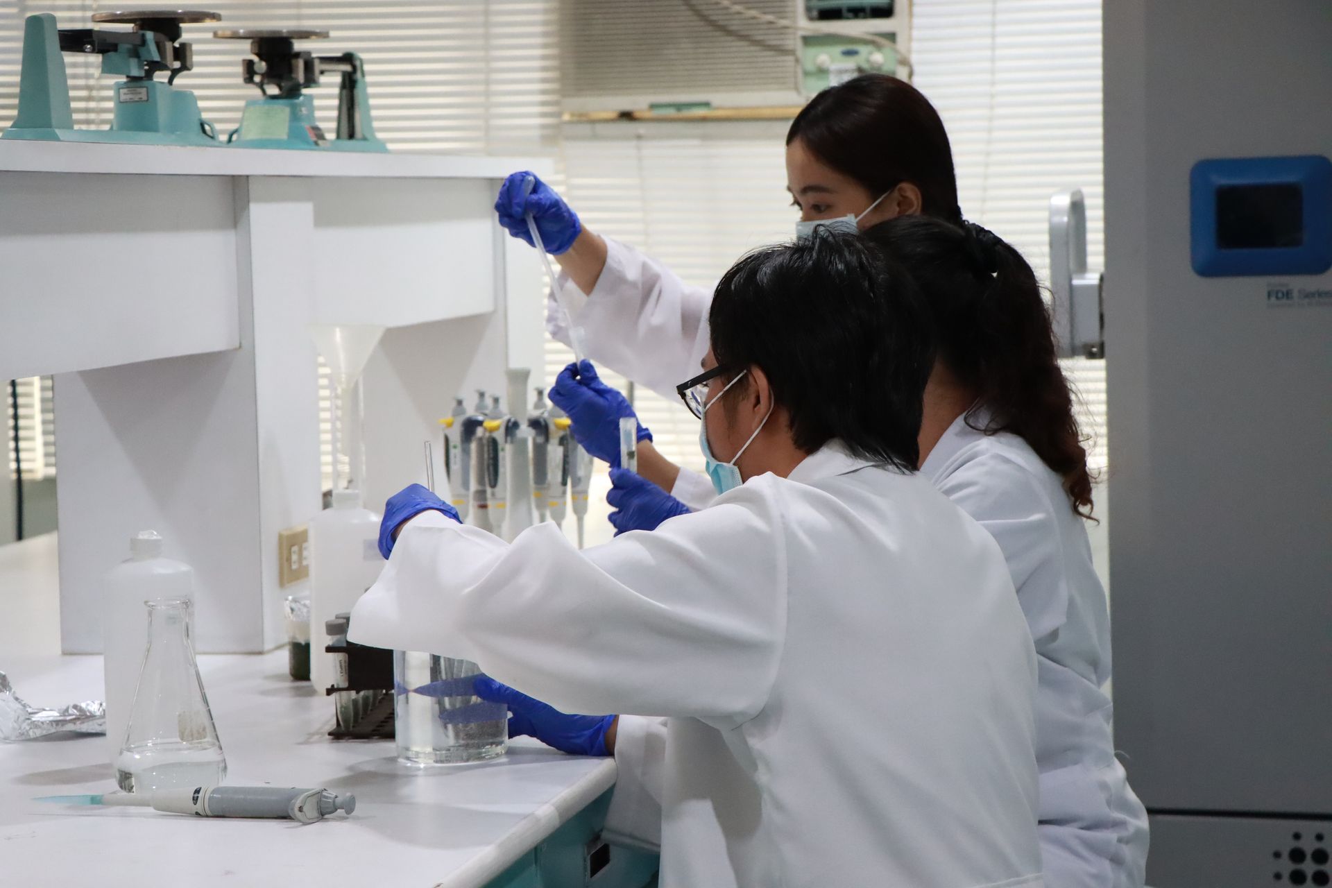 Scientists in white lab coats working with lab equipment in a bright laboratory
