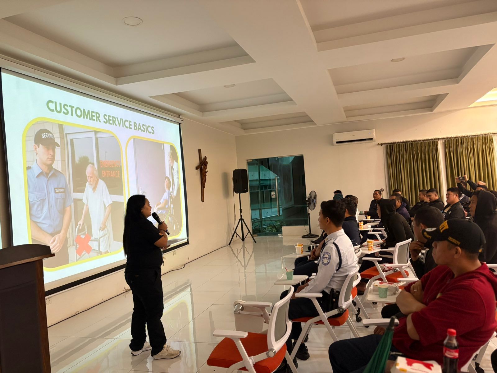 Presenter speaks to seated audience during a customer service training workshop in a bright classroom.