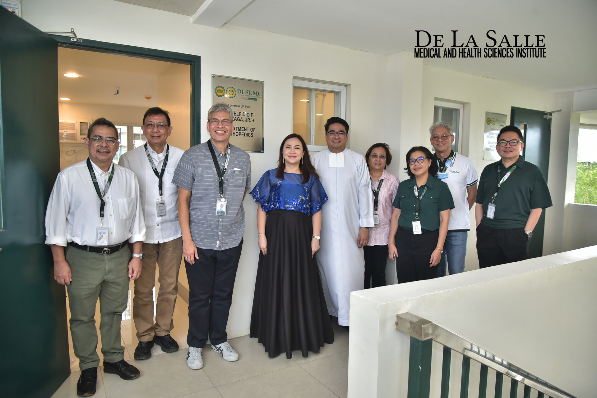 Seven people posing indoors in a hallway, with a De La Salle logo on the wall behind them.
