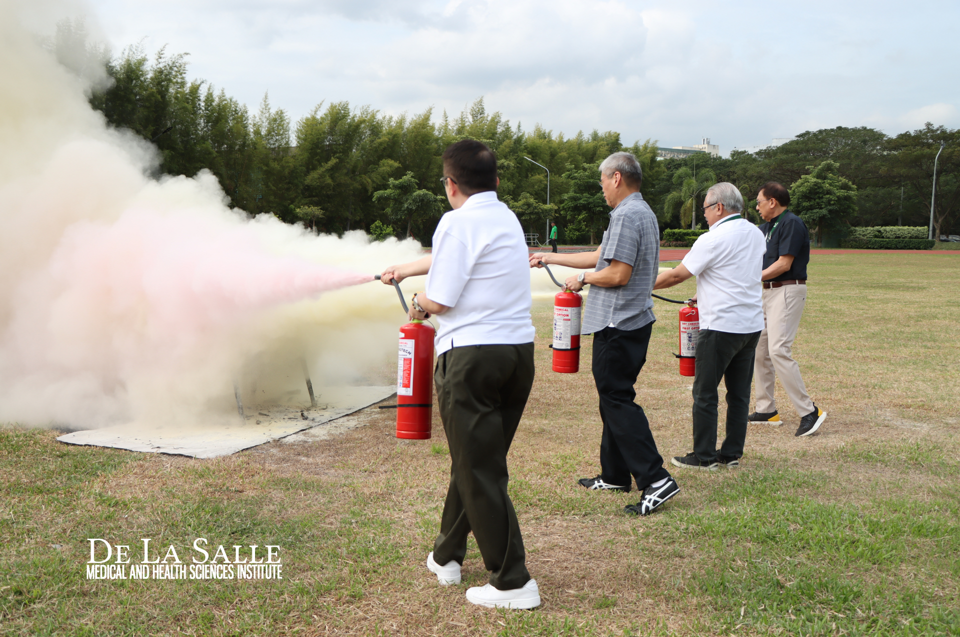 People using red fire extinguishers to spray a cloud of white foam on a grassy field