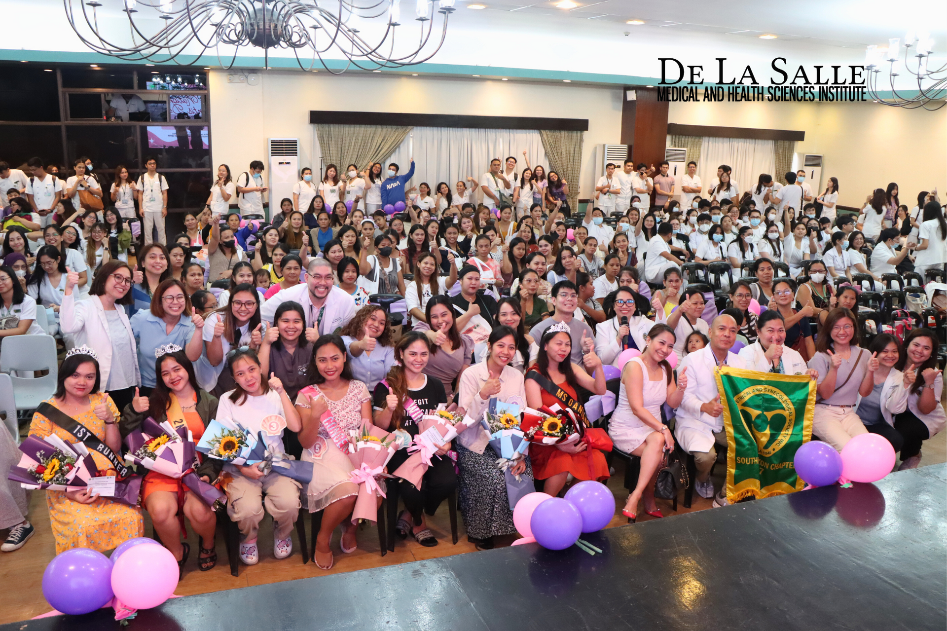 Large group posing indoors at a La Salle event, with pink balloons and a green banner in front.