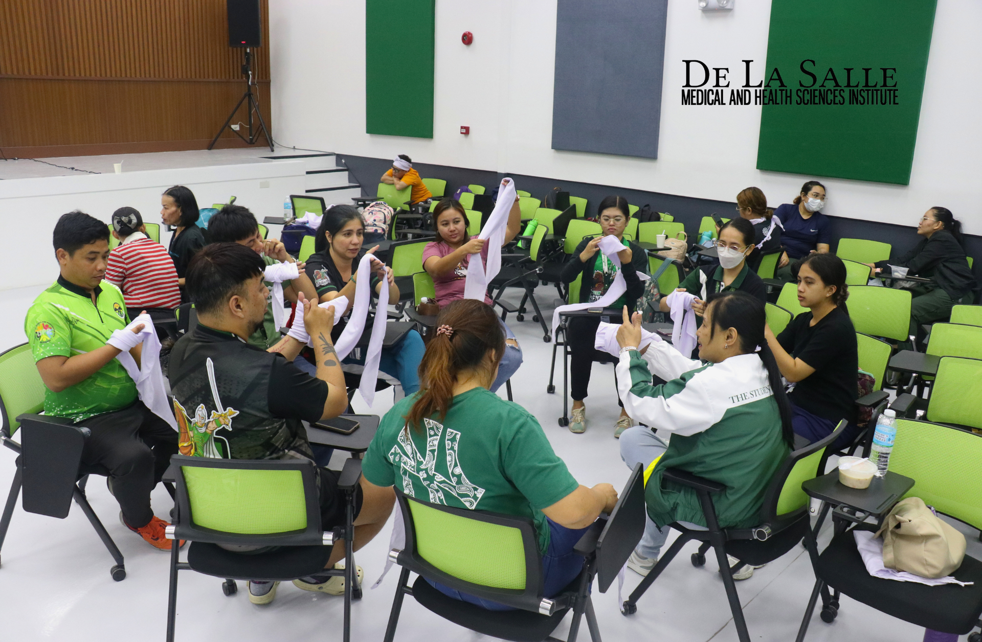 Group of people seated in a circle in a bright room, raising hands during a workshop or discussion.