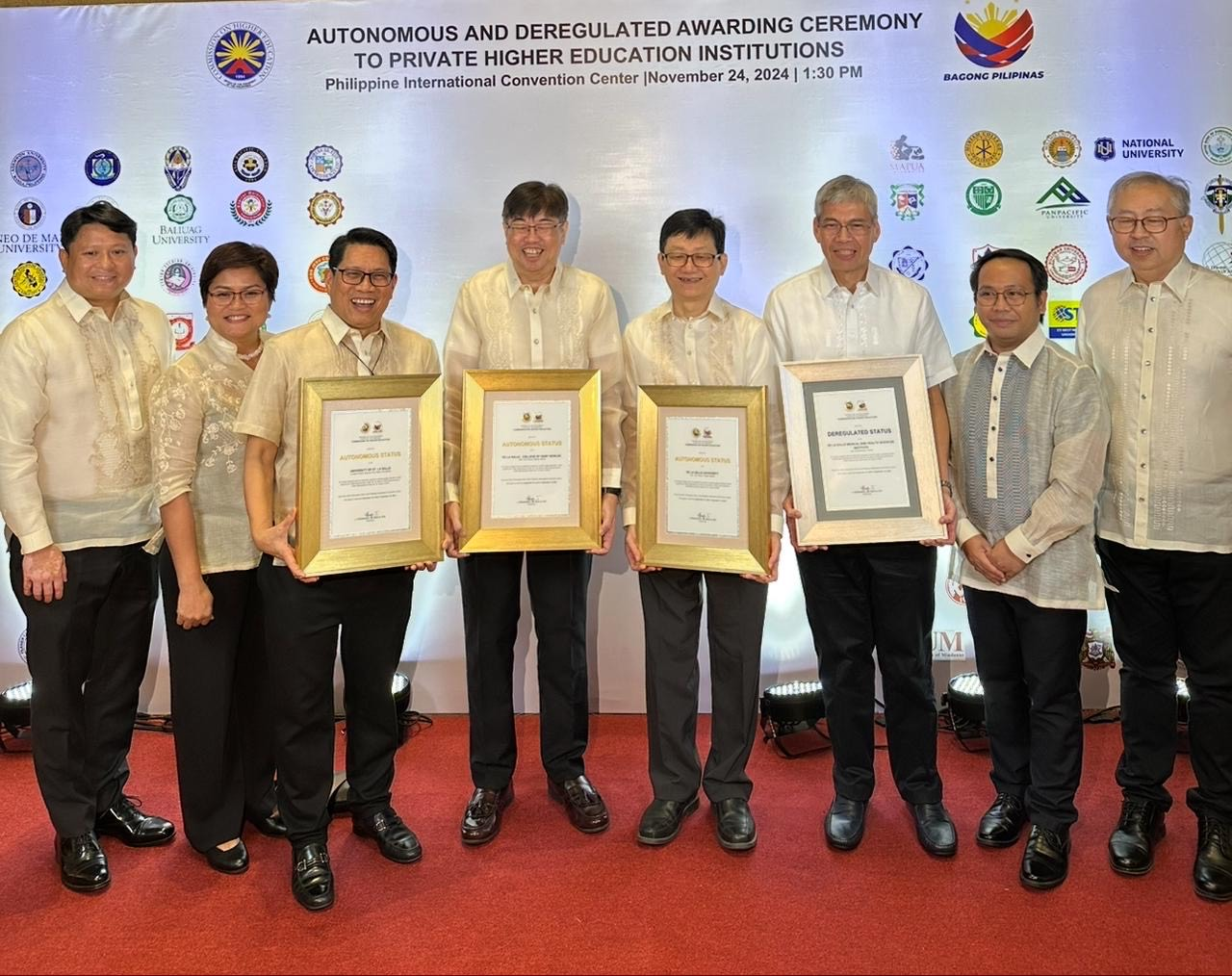 Eight people posing on a red carpet, holding framed awards at a formal ceremony backdrop