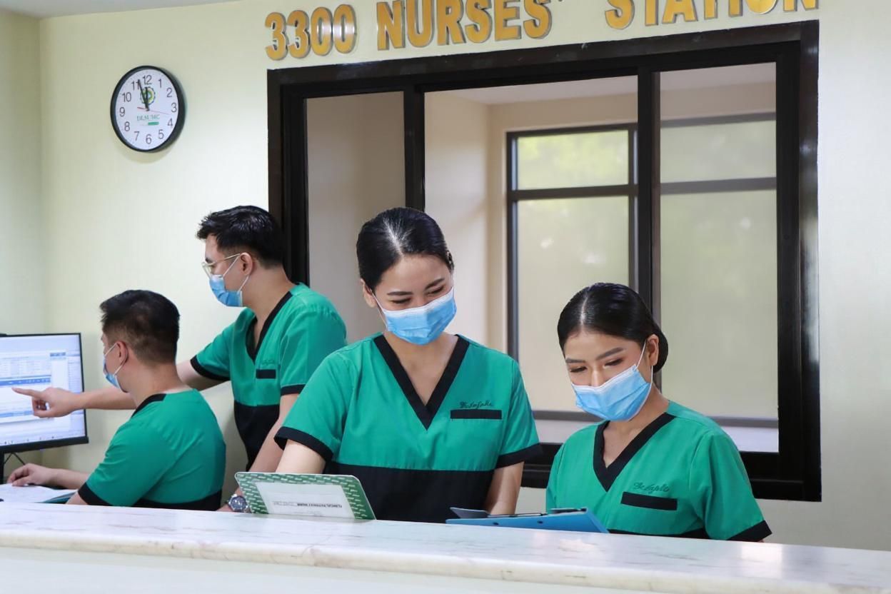 Nurses in green uniforms and masks working at a hospital station counter