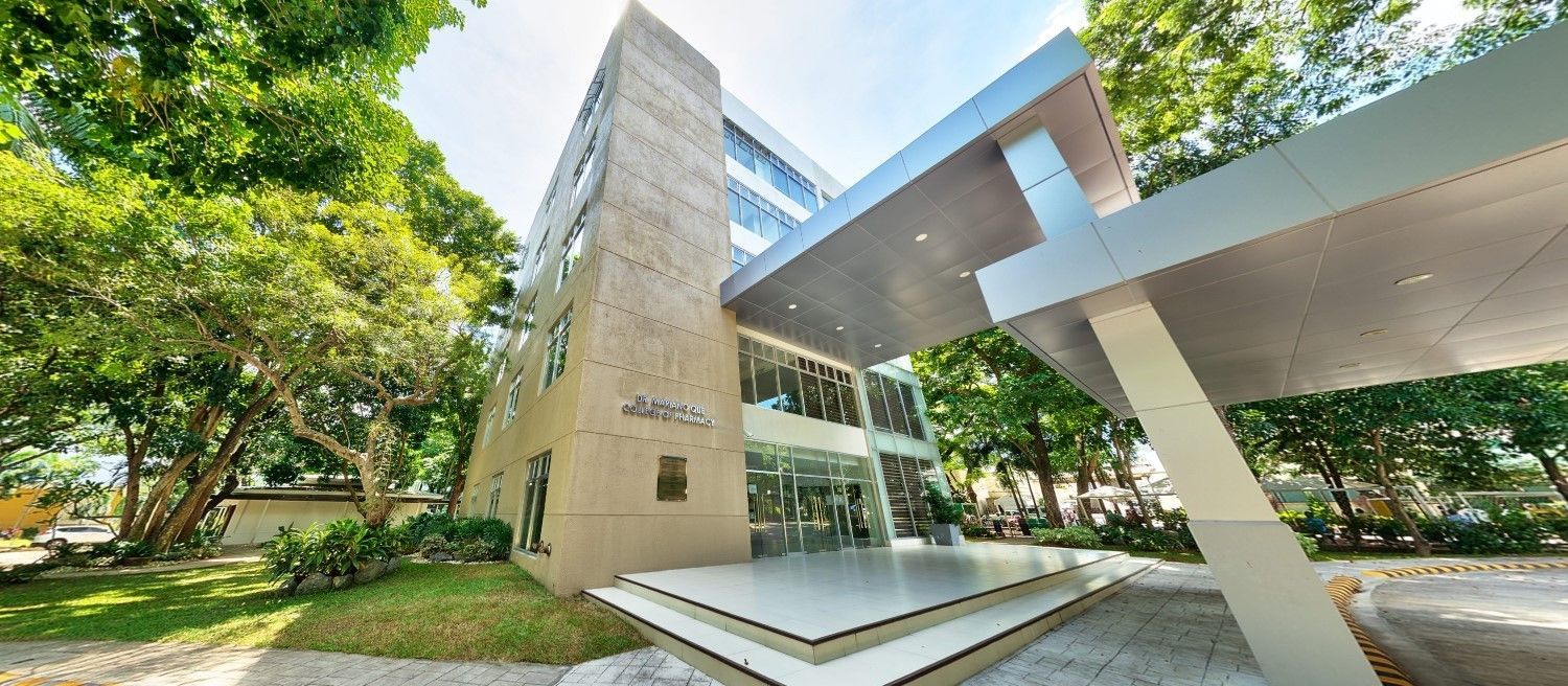 Modern building with glass facade, concrete towers, and a shaded walkway surrounded by green trees