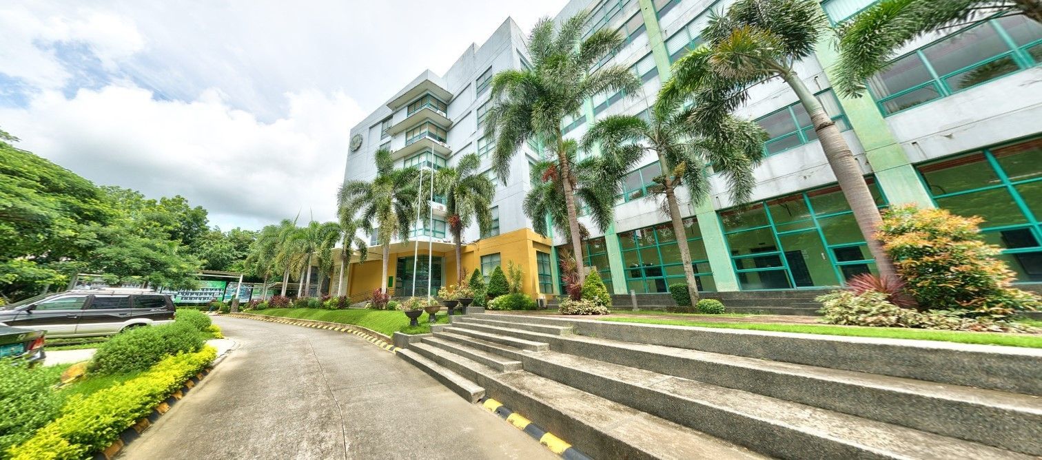 Modern office building with glass facade, palm trees, and a curved driveway under a cloudy sky