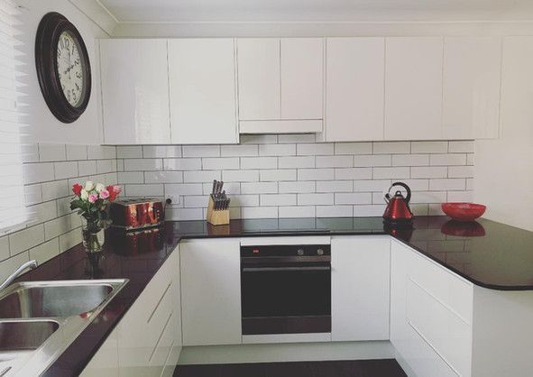 A kitchen with white cabinets and black counter tops and a clock on the wall.
