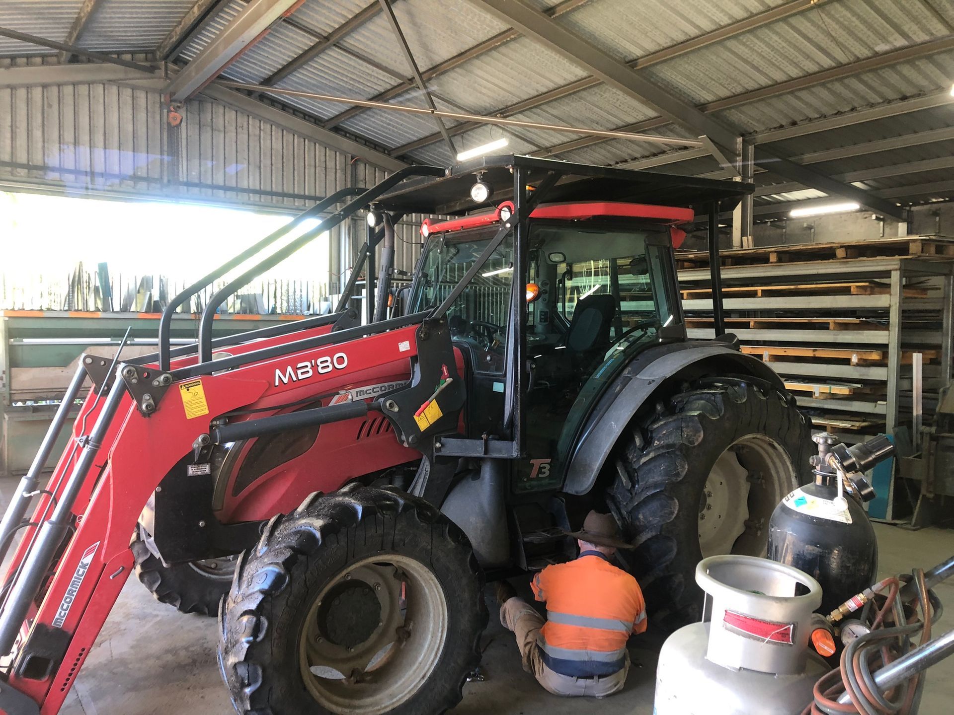 Red Tractor With A Front Loader And A Person Working On It — Soward Steel & Aluminium Fabrication in Kyogle, NSW