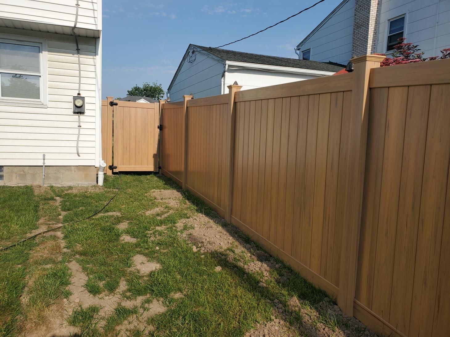 Spacious green lawn bordered by a new wooden fence, adorned with sturdy stone brick pillars.