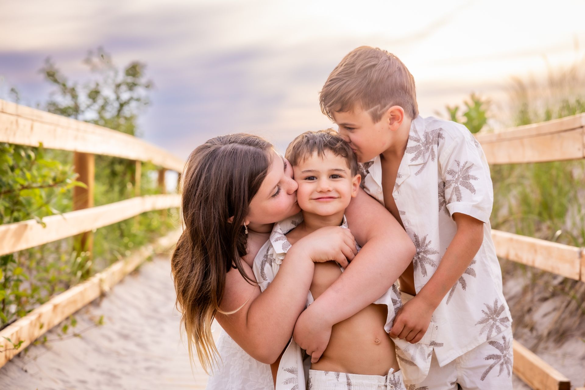 Three children hugging on a sunlit wooden bridge outdoors