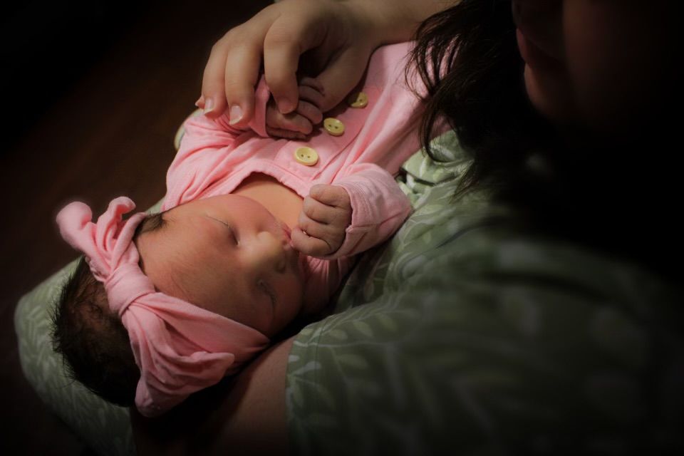 Sleeping baby in pink headband, resting on an adult's chest.