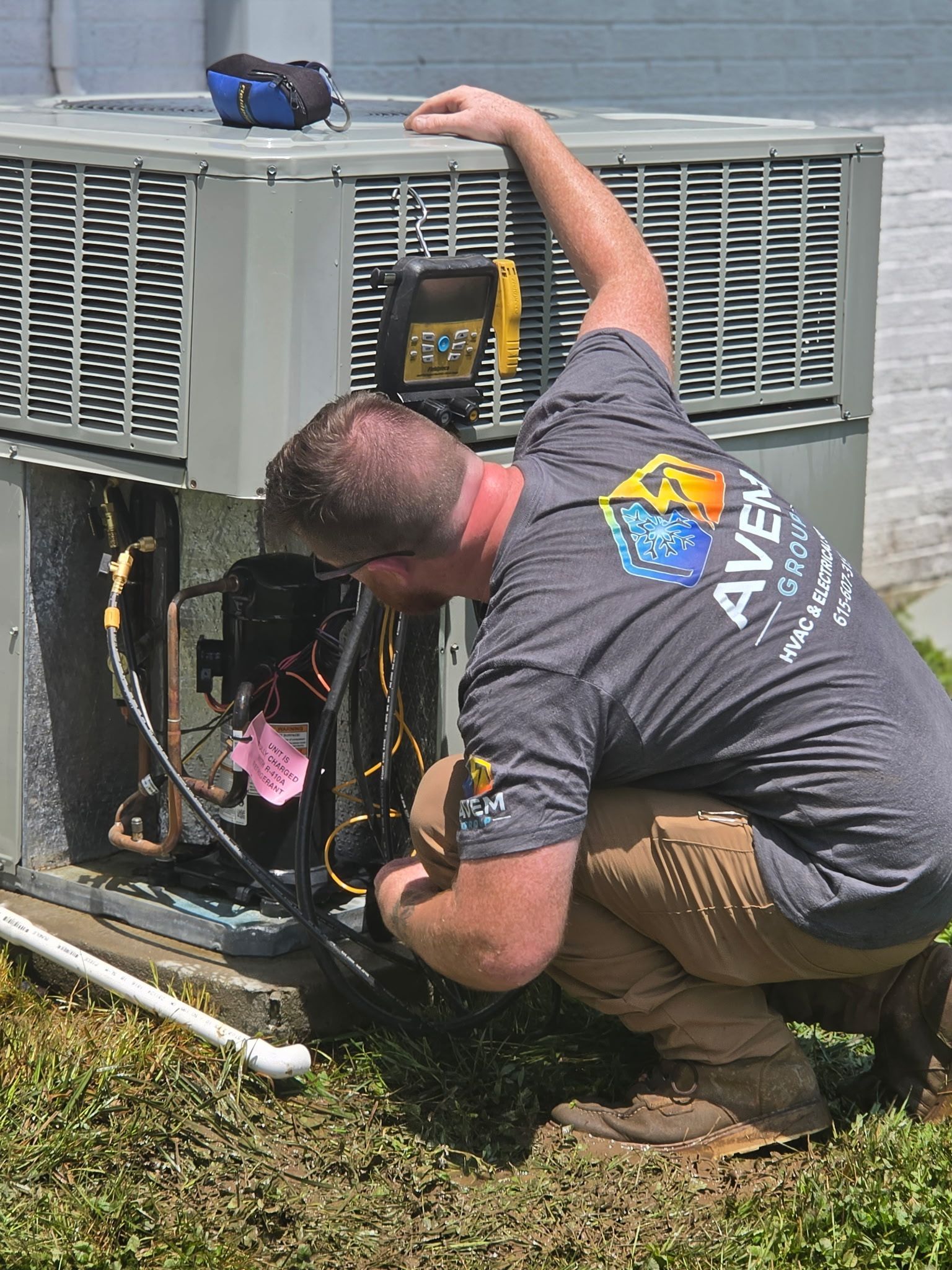 Technician servicing an outdoor HVAC unit on grass, using tools with the panel open
