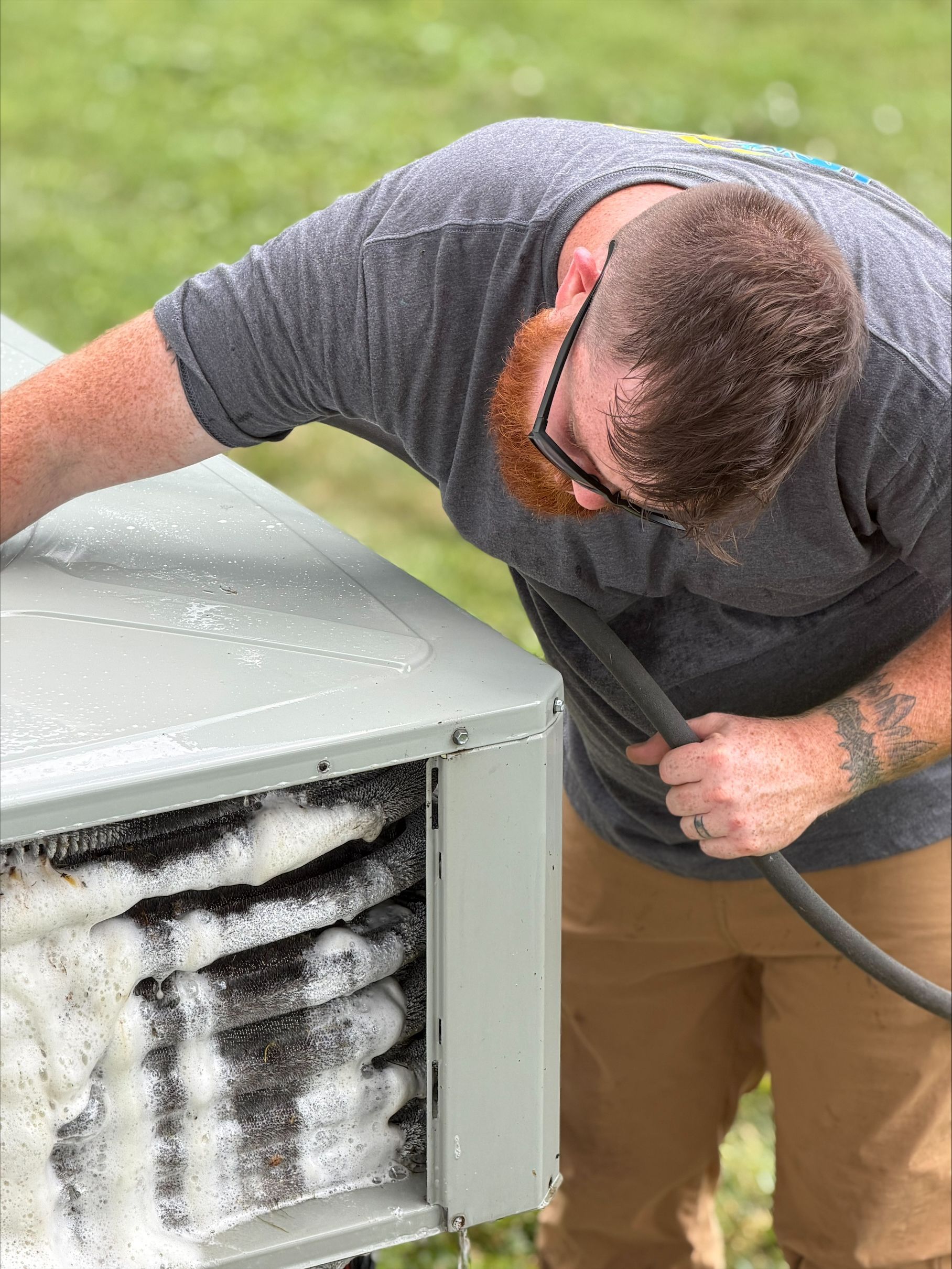 Technician cleaning snow or ice from an outdoor HVAC unit with a hose