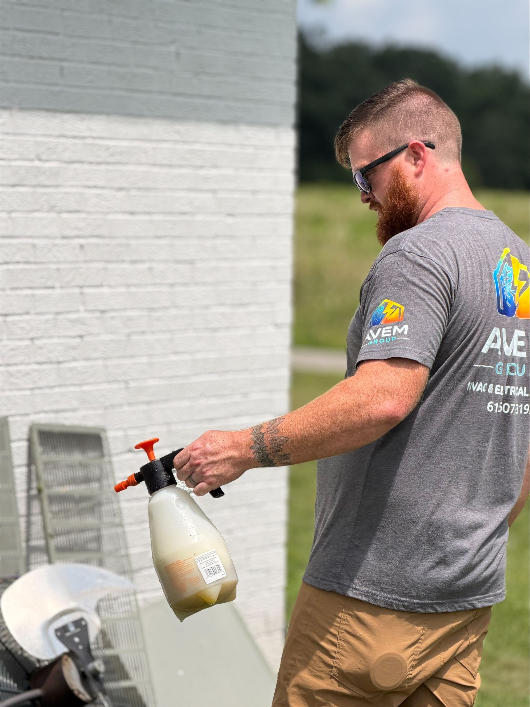 Man in gray T-shirt using a spray bottle to clean a white chair outdoors beside a building.
