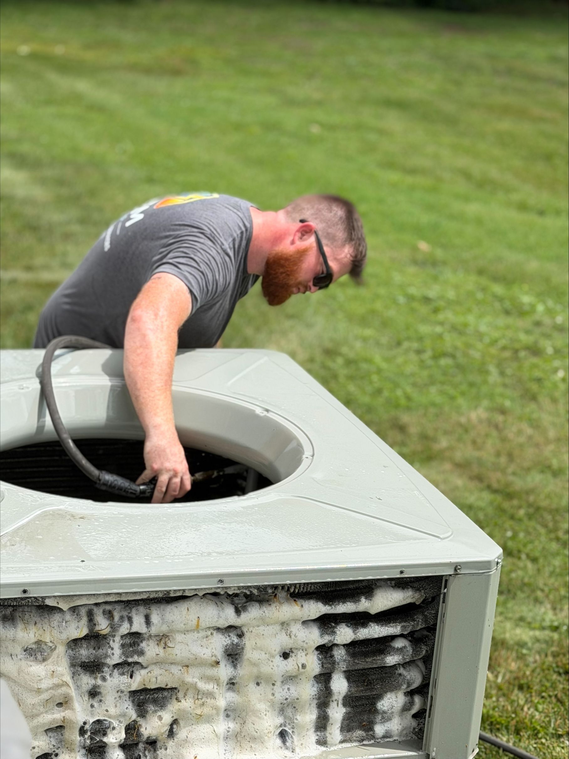 Person leaning into a large outdoor HVAC unit on a grassy lawn