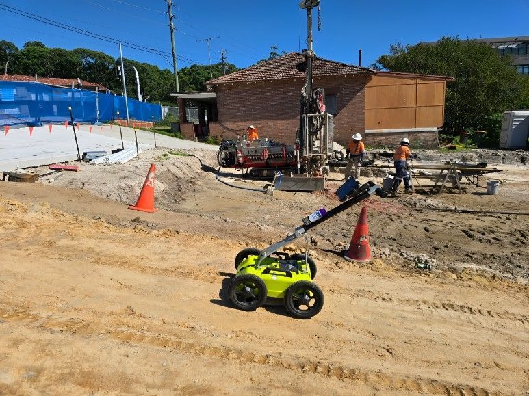 A lime green robot on a construction site with workers, drilling rig, and a brick building.