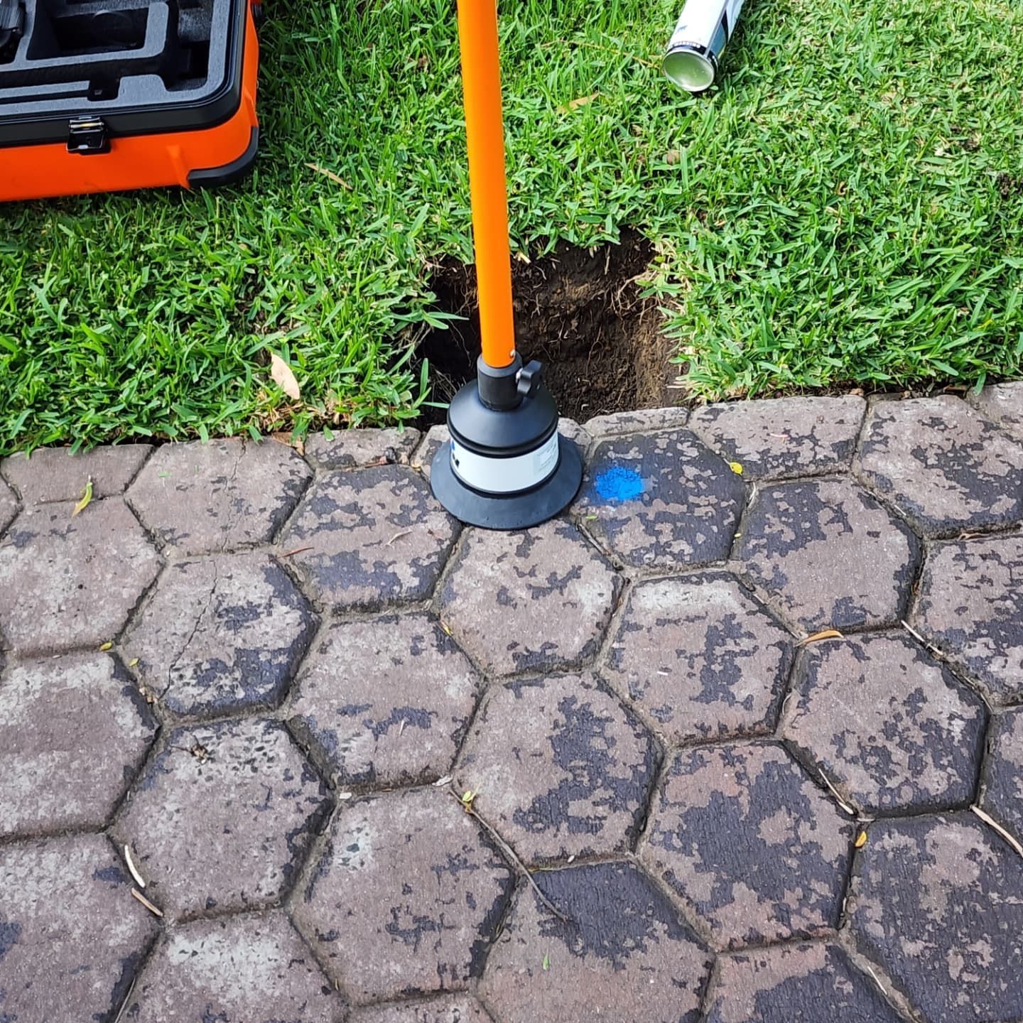 Orange tool in hole in lawn next to a brick path.