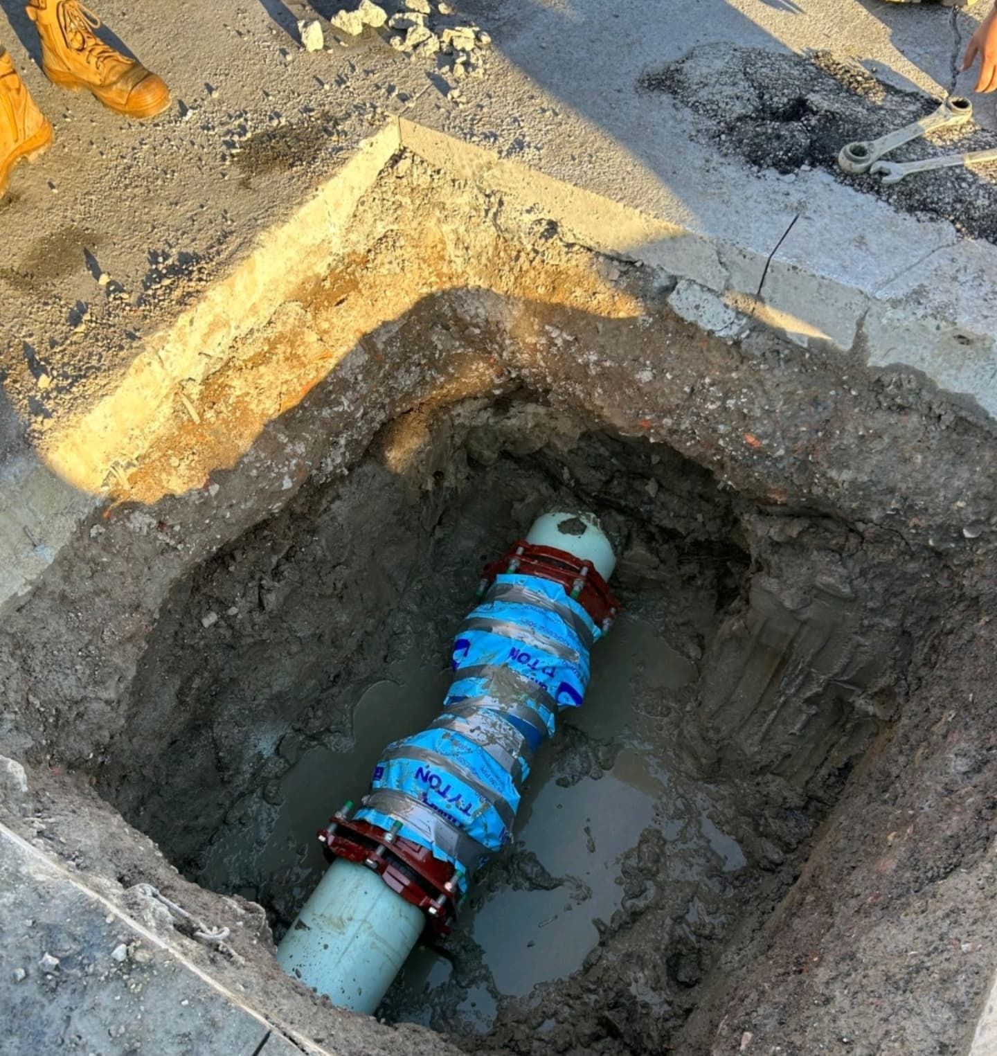 A water pipe replacement in a concrete-lined hole. Blue couplings, reddish connectors, muddy setting.
