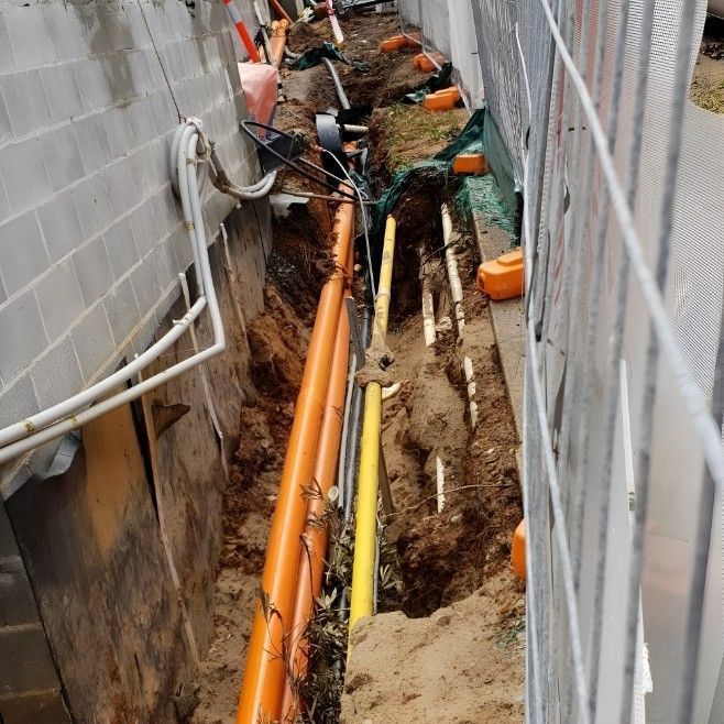 Leaking green pipe connected with copper fitting in a wall; water spraying.