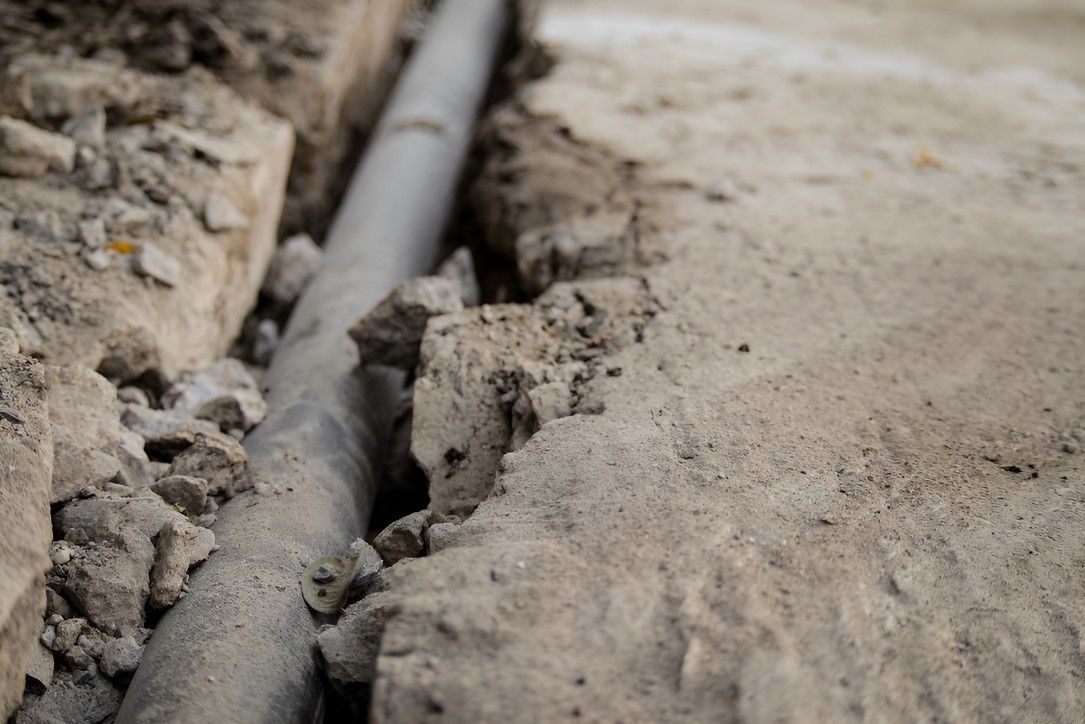 Gray pipe in a narrow trench dug in sandy soil.