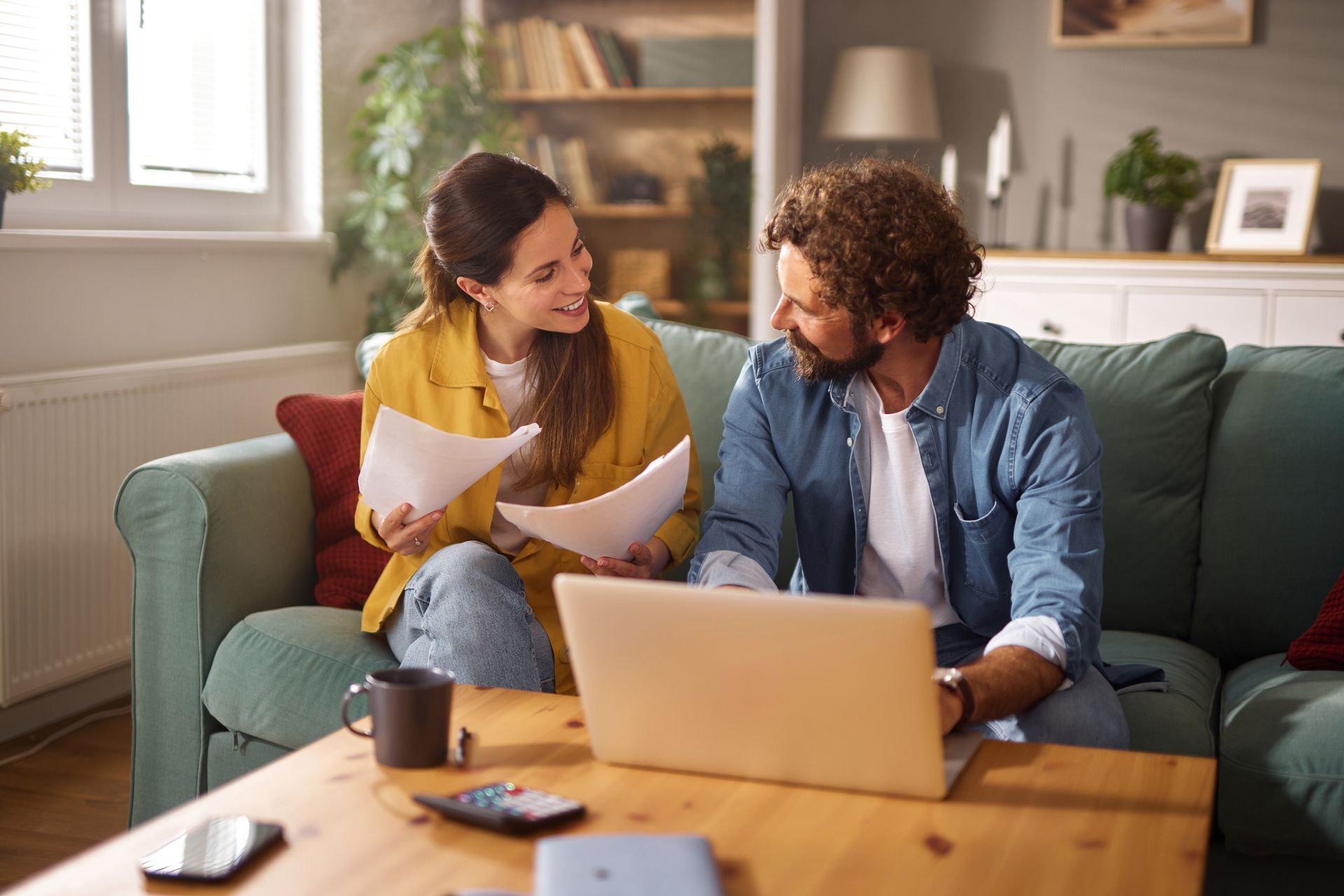 Two people smiling and talking on a couch with a laptop in a cozy living room