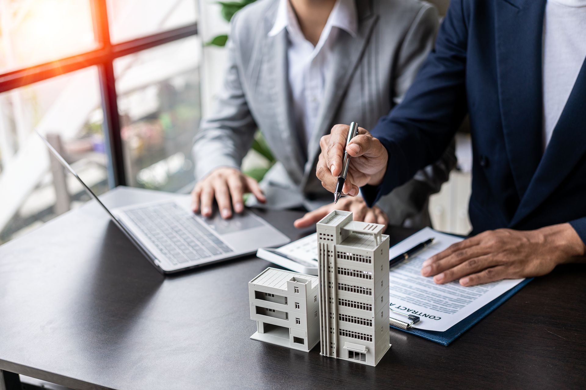 Two people reviewing a building model and plans beside a laptop in an office meeting