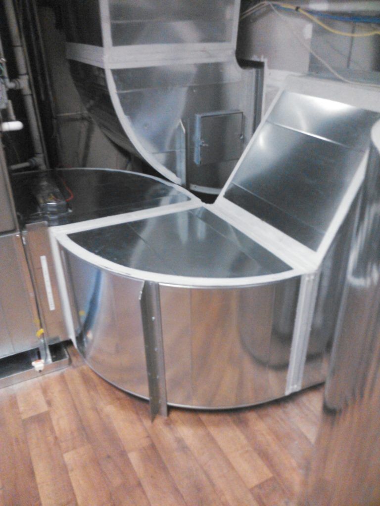 Galvanized metal HVAC ductwork, round and angular shapes, on a wood floor.