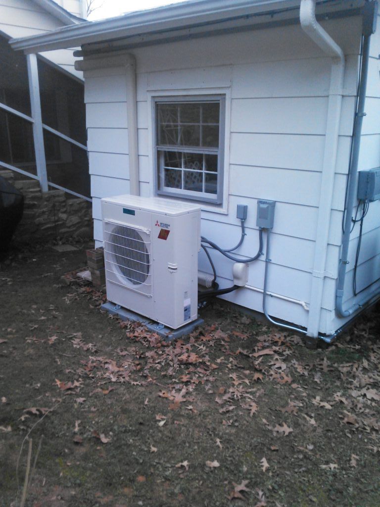 White heat pump unit next to a white building with a window, on a grassy patch.