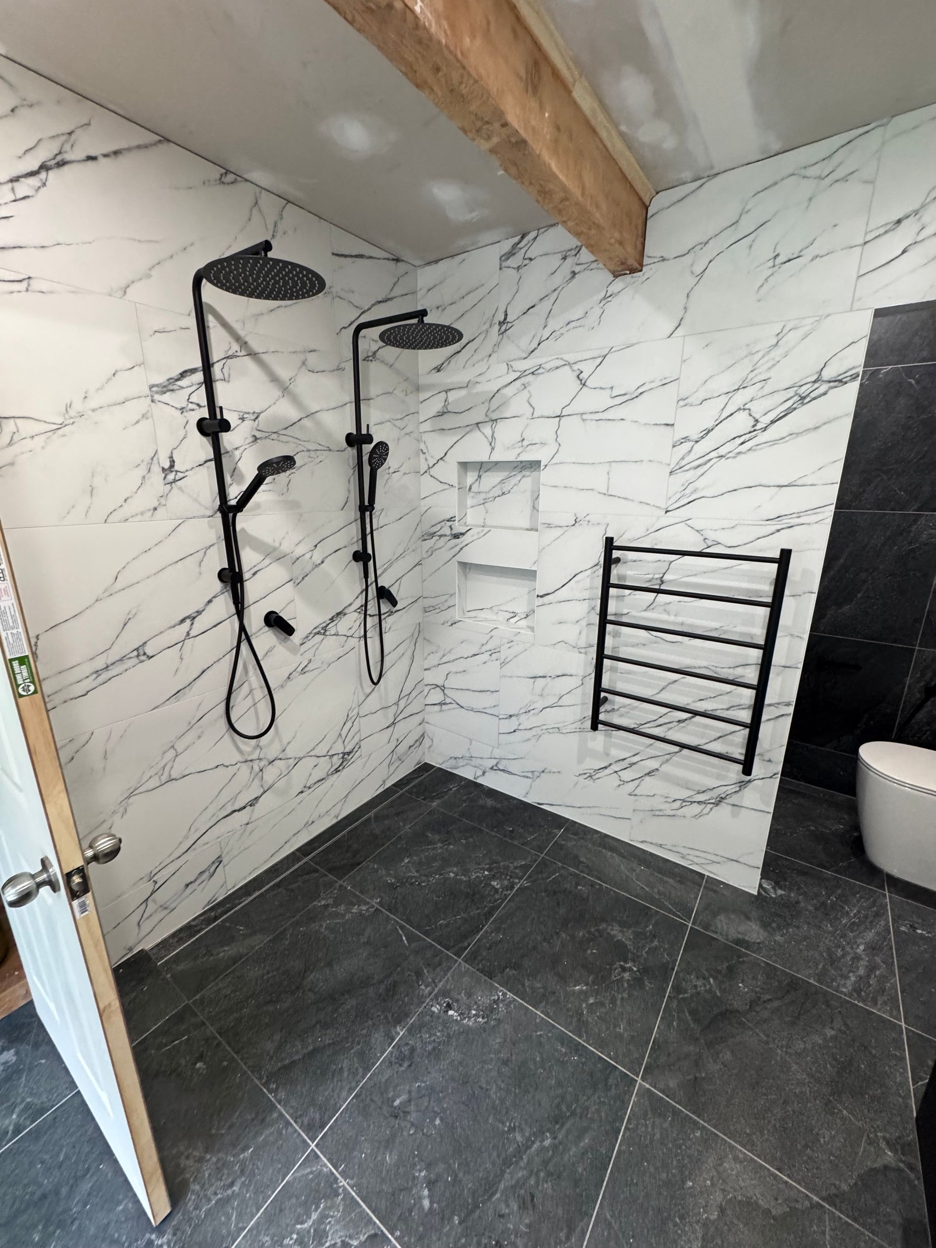 Bathroom with black fixtures, marble-patterned walls, dark tile floor, black towel rack, and a toilet  — Fair Plumbing In Shellharbour, NSW